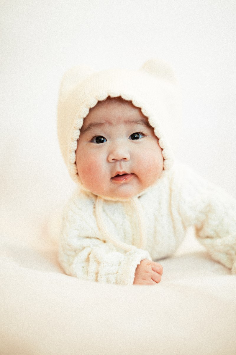 Baby in a cream bonnet looking toward the camera during tummy time.