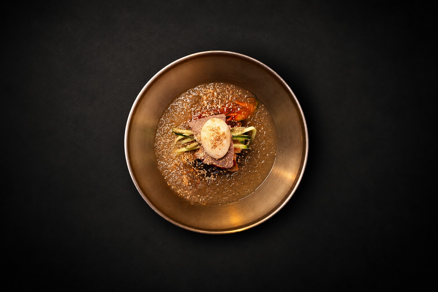 Noodles, sliced meat, cucumber, and egg in a golden bowl