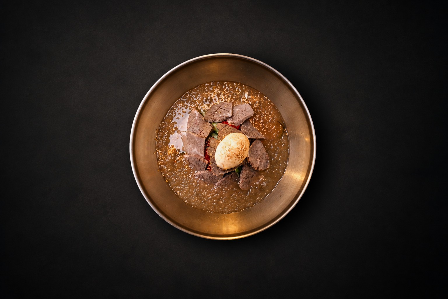 A golden bowl with noodles, sliced meat, and a halved egg