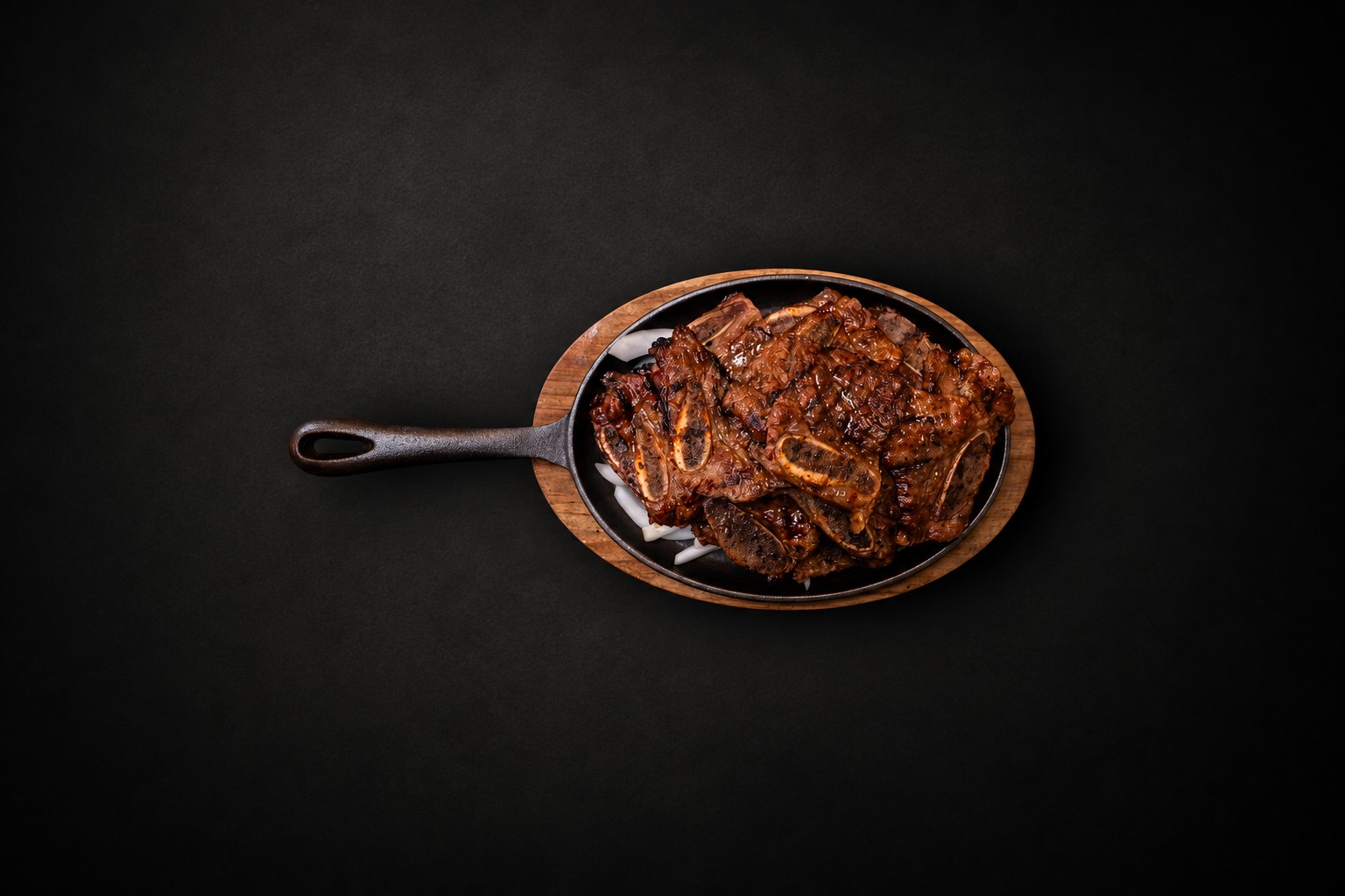 Grilled meat on a dark sizzling platter and wooden board
