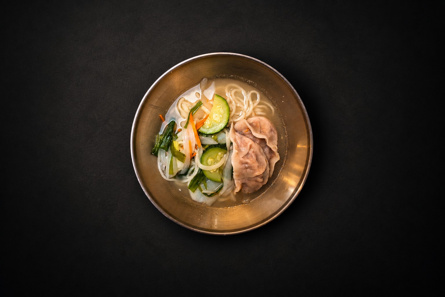 Noodles, dumplings, and vegetables in a golden bowl