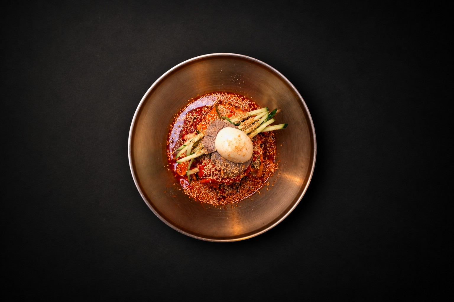 A golden bowl of red noodles and fresh cucumber
